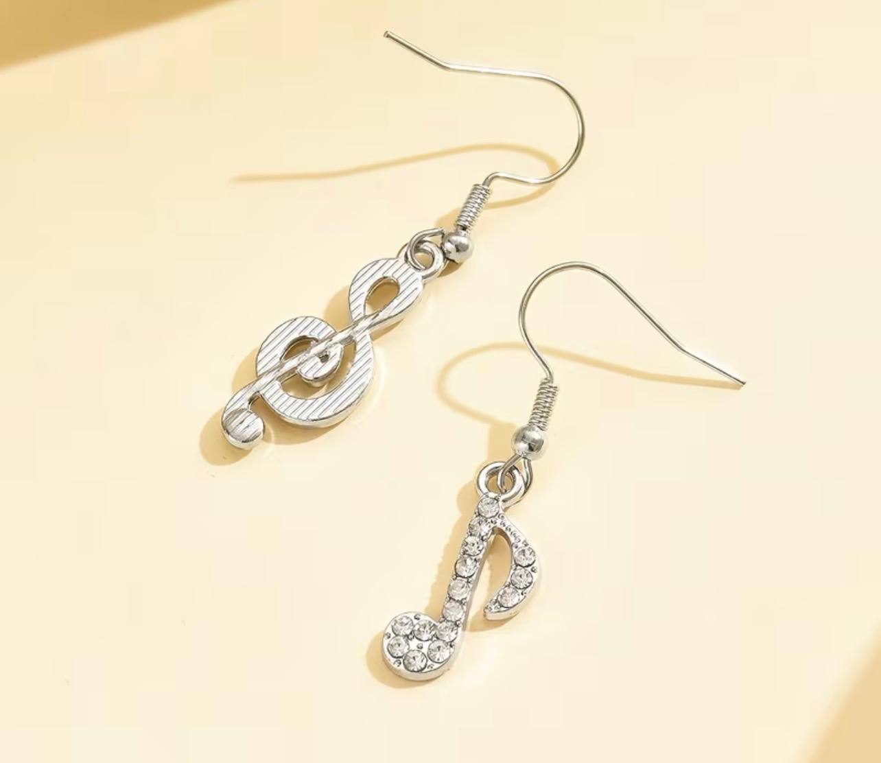 Music Note Crystal Earrings — silver pair flat lay on cream background