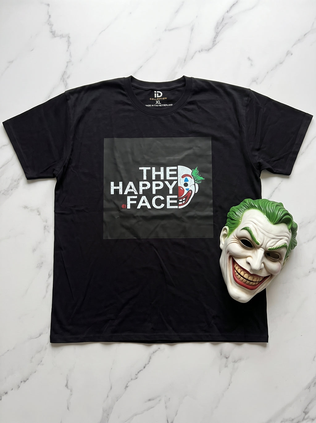 The Happy Face Tee — black oversized t-shirt with Joker graphic print, flat lay on marble