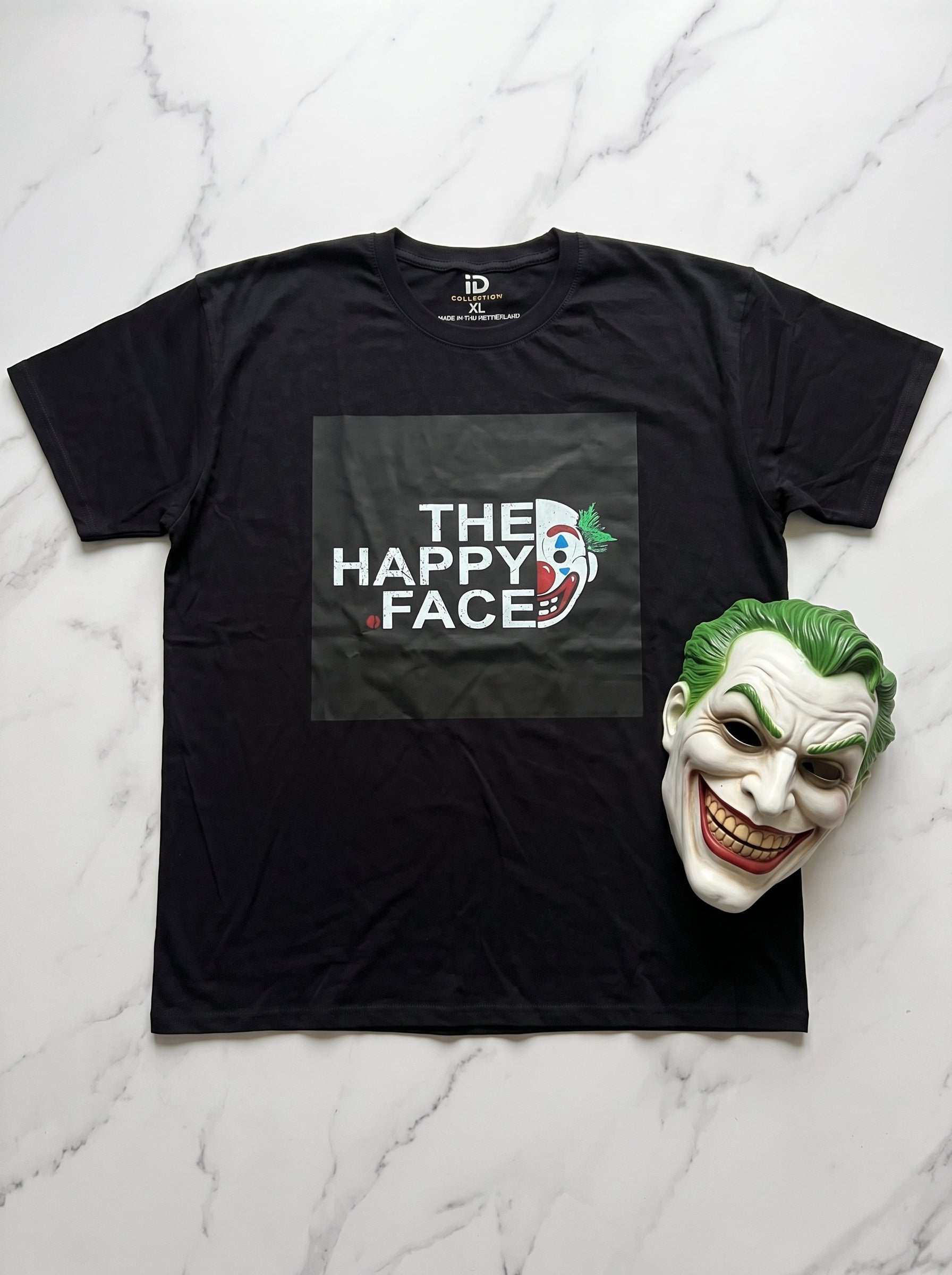 The Happy Face Tee — black oversized t-shirt with Joker graphic print, flat lay on marble