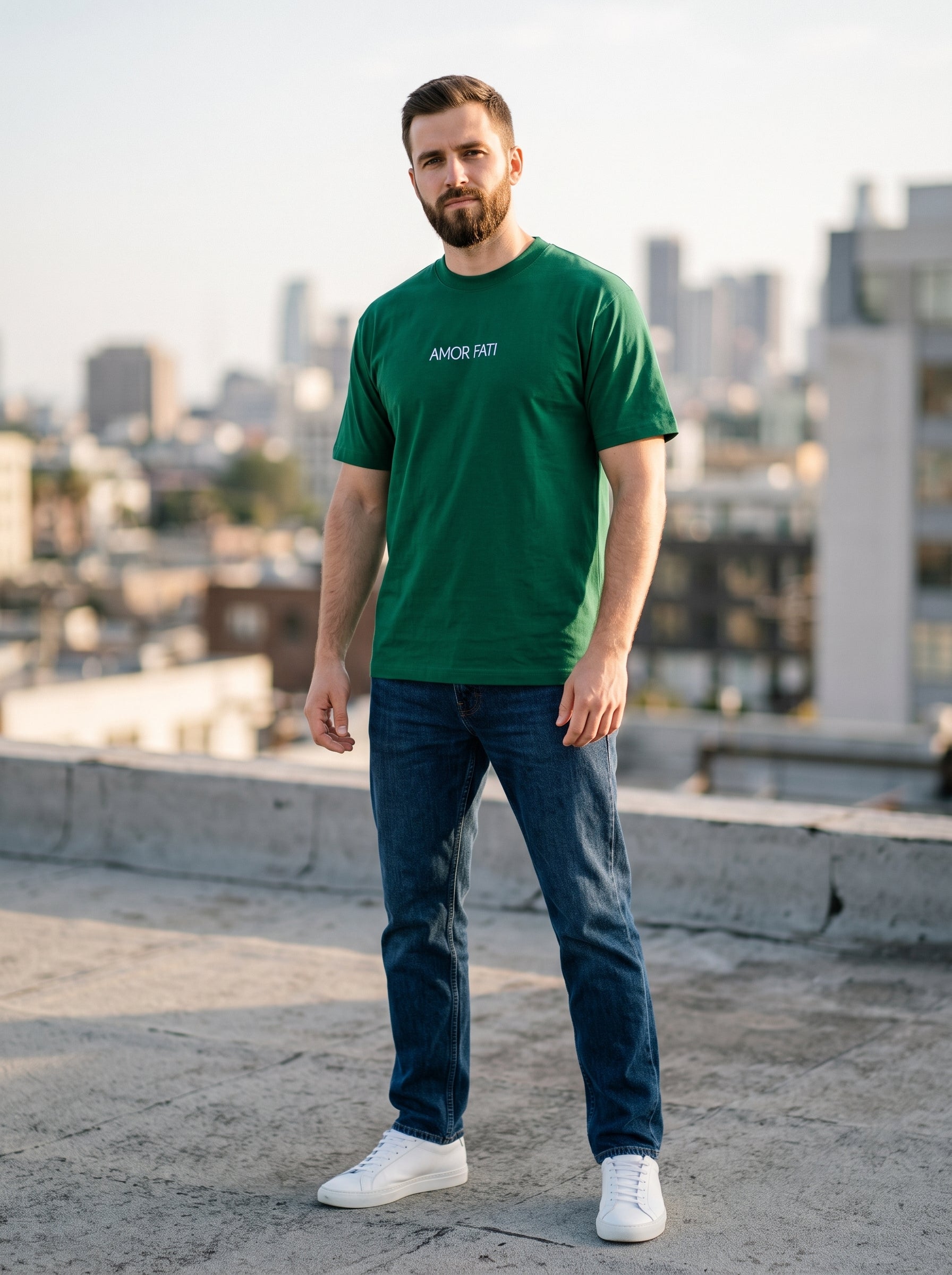 Amor Fati Tee — forest green t-shirt with minimal white AMOR FATI chest print worn by man on rooftop