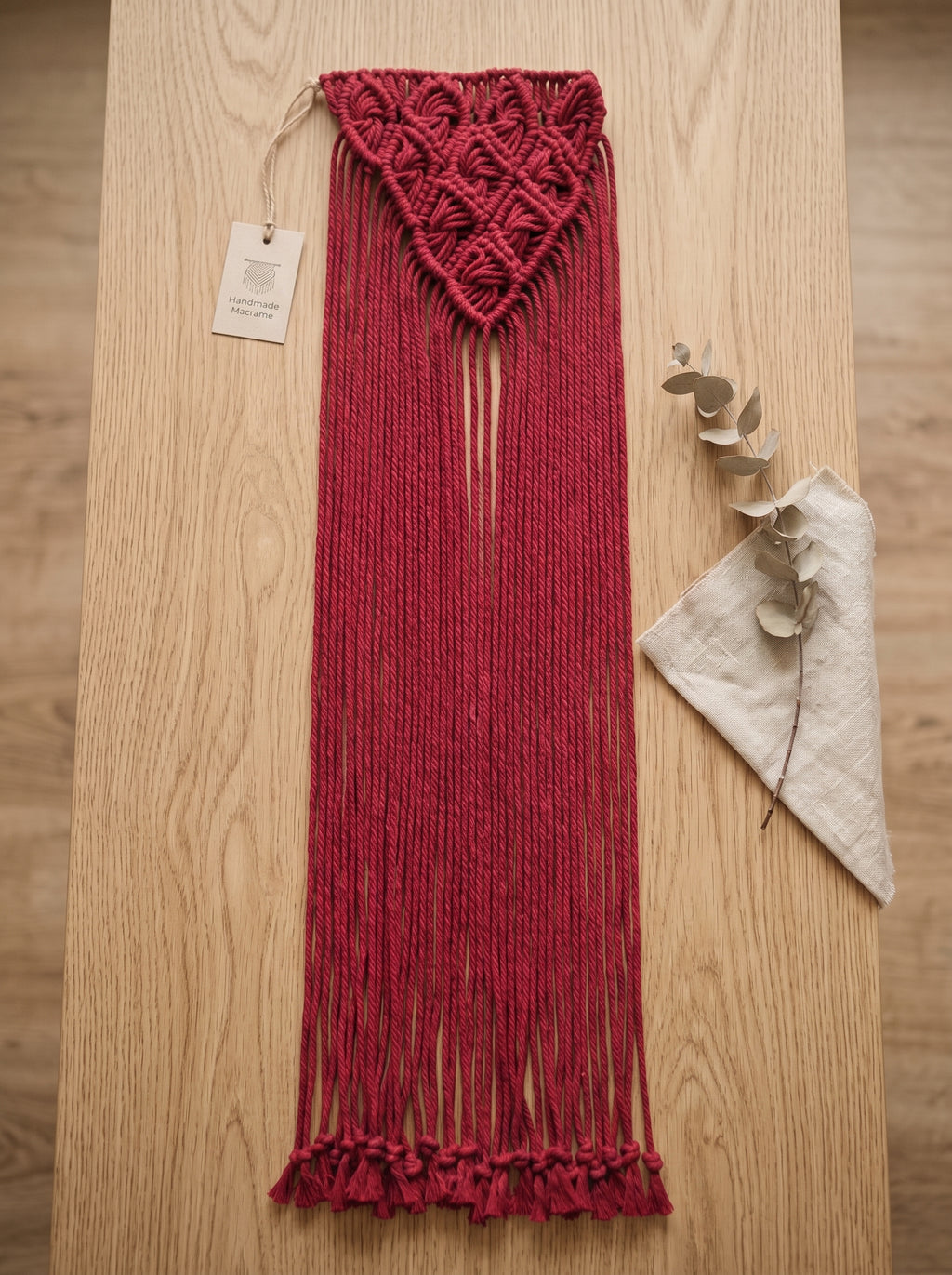 Macrame Fringe Belt in Burgundy — flat lay on wooden surface with eucalyptus branch