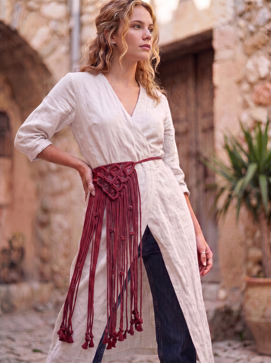 Macrame Fringe Belt in Burgundy — worn by model over white dress in Mediterranean setting